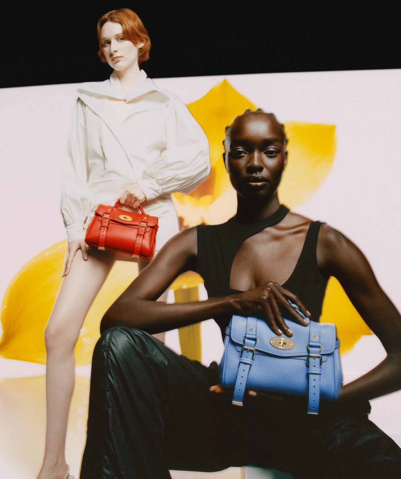 Two models holding the Mini Alexa handbag in Cornflower Blue and Coral Orange